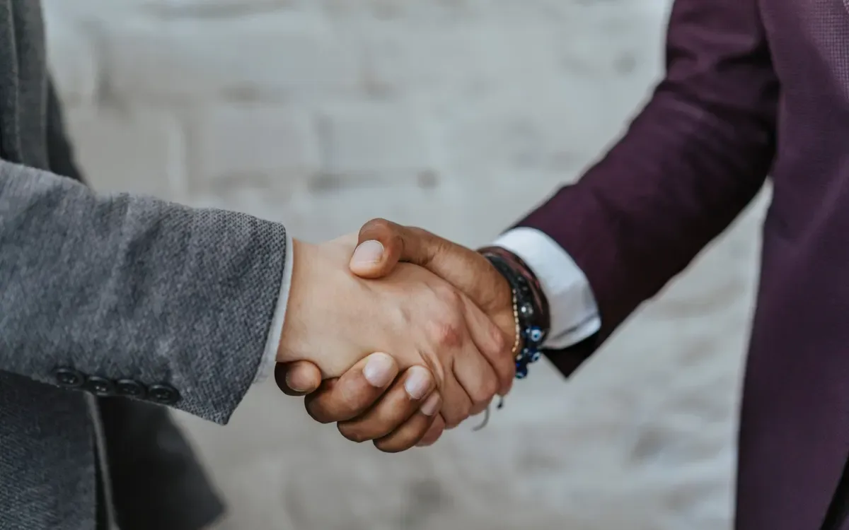 Two people in suit jackets, one grey and one plum, shaking hands